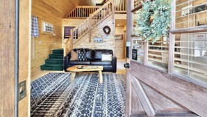 A wooden interior with a staircase, a black leather sofa, and a patterned rug. - Juniper Grove | Loft & Personal Hot Tub! (Overgaard)