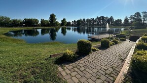 A tranquil outdoor setting with a pond, a wooden dock, and a clear blue sky. - Juniper Grove | Loft & Personal Hot Tub! (Overgaard)
