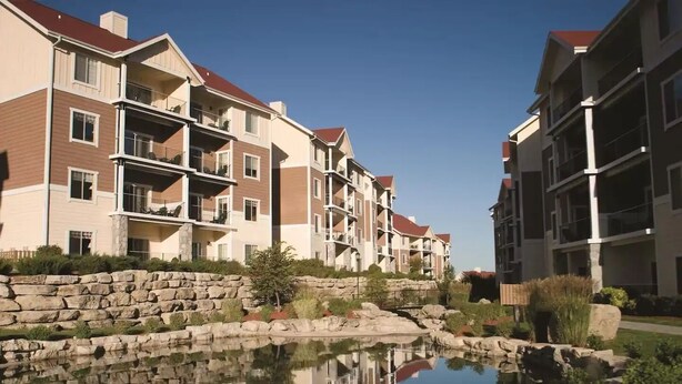 A multi-story residential building with balconies, a stone retaining wall, and a small pond reflecting the buildings. - Wyndham Vacation Resort! Serene · Clean · Fun! (Branson)