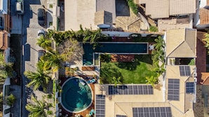 Vue aérienne d’un quartier résidentiel avec une piscine, des panneaux solaires et une pelouse bien entretenue.