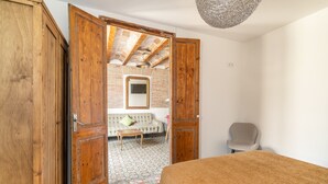Un dormitorio con un armario de madera, una cama, una silla, un sofá y suelo de baldosas.