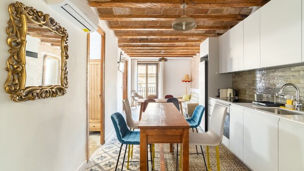 Un comedor con una mesa y sillas de madera, una cocina con salpicadero de ladrillo y un espejo grande y decorativo en la pared.