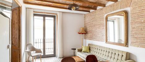 Una habitación con vigas de madera a la vista, un espejo grande, un sofá, una silla y un suelo con diseño.