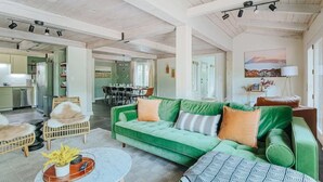 A spacious living area with a green sofa, wicker chairs, and a dining table in the background.