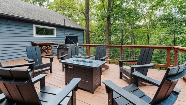 A deck with outdoor seating and a fire pit, surrounded by trees.