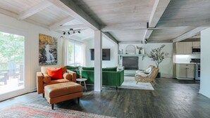 A spacious living area with a sofa, a green armchair, and a fireplace. There is a kitchen in the background.