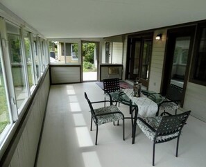 Eira coberta com mesa e cadeiras, janelas amplas e vista para o exterior.