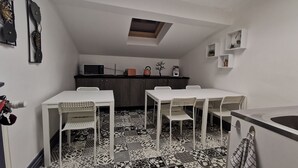 A compact kitchen with a microwave, toaster, and kettle on the counter. There is a dining table with four chairs, and the floor has patterned tiles. - Nuit tendance à Mâcon (Mâcon)