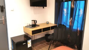 A compact hotel room with a bed, a desk with a coffee maker, a TV, and a small fridge. - Nuit tendance à Mâcon (Mâcon)