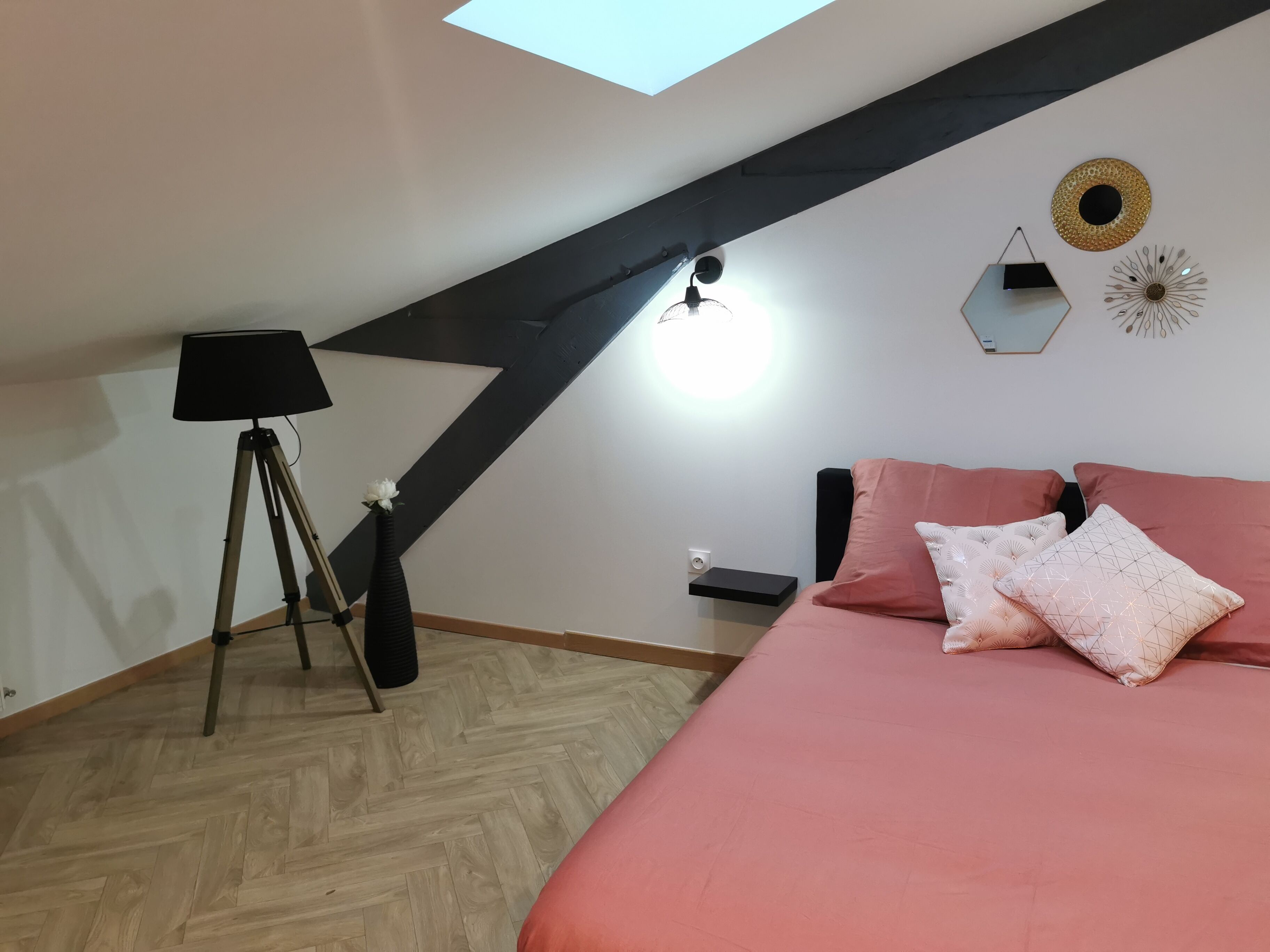 Un dormitorio con techo inclinado, una cama con ropa de cama rosa, una lámpara y adornos en la pared.