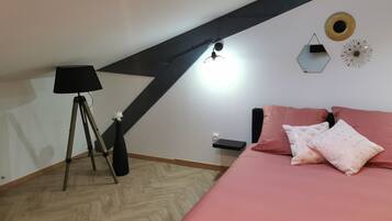 Un dormitorio con techo inclinado, una cama con ropa de cama rosa, una lámpara y adornos en la pared.