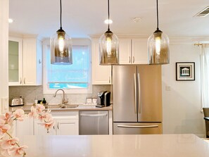 Cocina moderna con armarios blancos, electrodomésticos de acero inoxidable e iluminación colgante.