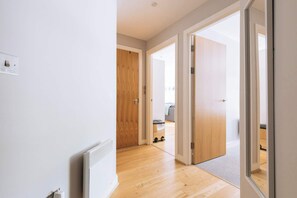 Ein Flur mit Holzboden, einem Heizkörper und einer Tür zu einem Raum mit einem grauen Sofa.