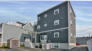 A multi-story residential building with a garage, a small shed, and a fenced driveway. - Sleek Somerville Apartment near Encore! (Somerville)