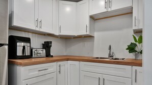 A modern kitchen with white cabinets, a wooden countertop, a coffee maker, a toaster, and a sink. - Sleek Somerville Apartment near Encore! (Somerville)