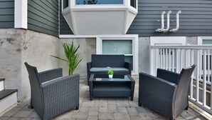 An outdoor patio with wicker furniture, a small table with a plant, and a window above. - Sleek Somerville Apartment near Encore! (Somerville)
