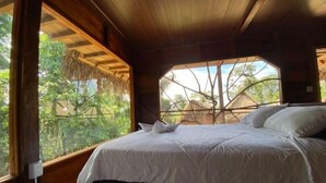 Un lit recouvert de draps blancs, dans une pièce aux murs en bois et dotée d’une grande fenêtre.