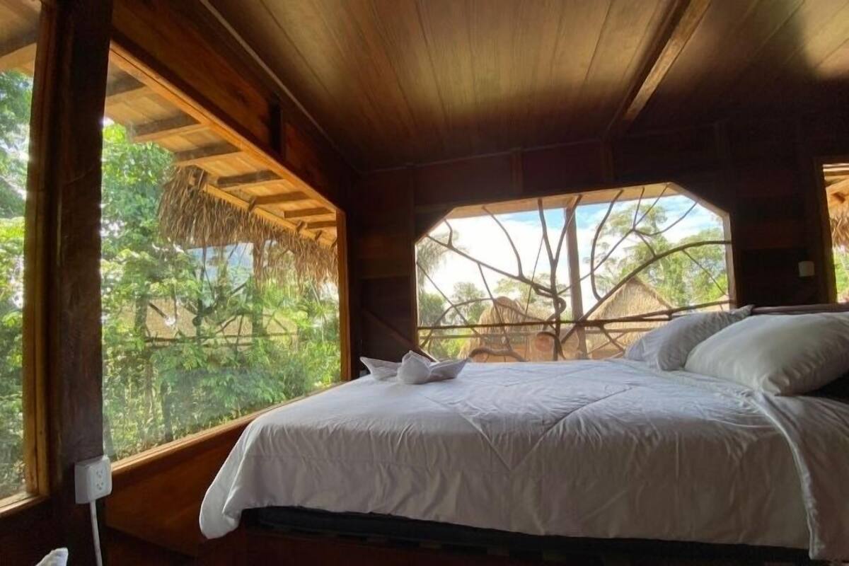 A bed with white linens in a room with wooden walls and a large window.