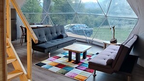 A spacious tent interior with a wooden staircase, a dark sofa, a colorful rug, and a hanging light fixture.