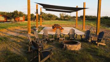 A rustic outdoor seating area with Adirondack chairs, a fire pit, and a wooden table.