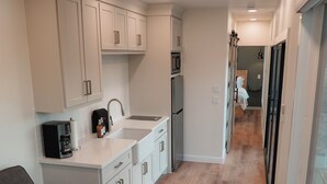 A compact kitchen with white cabinets, a built-in microwave, and a sink. A gray sofa is positioned in the foreground. - Trout Container Home - Fish Camp Rockport (Rockport)