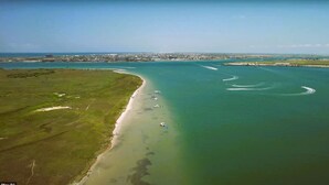 An aerial view of a coastal area with a beach, boats, and a distant cityscape. - Trout Container Home - Fish Camp Rockport (Rockport)
