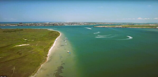 An aerial view of a coastal area with a beach, boats, and a distant cityscape.