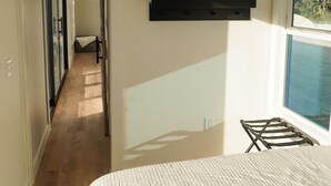 A bedroom with a large bed, a mounted TV, a window with a view, and a hallway leading to another room. - Trout Container Home - Fish Camp Rockport (Rockport)