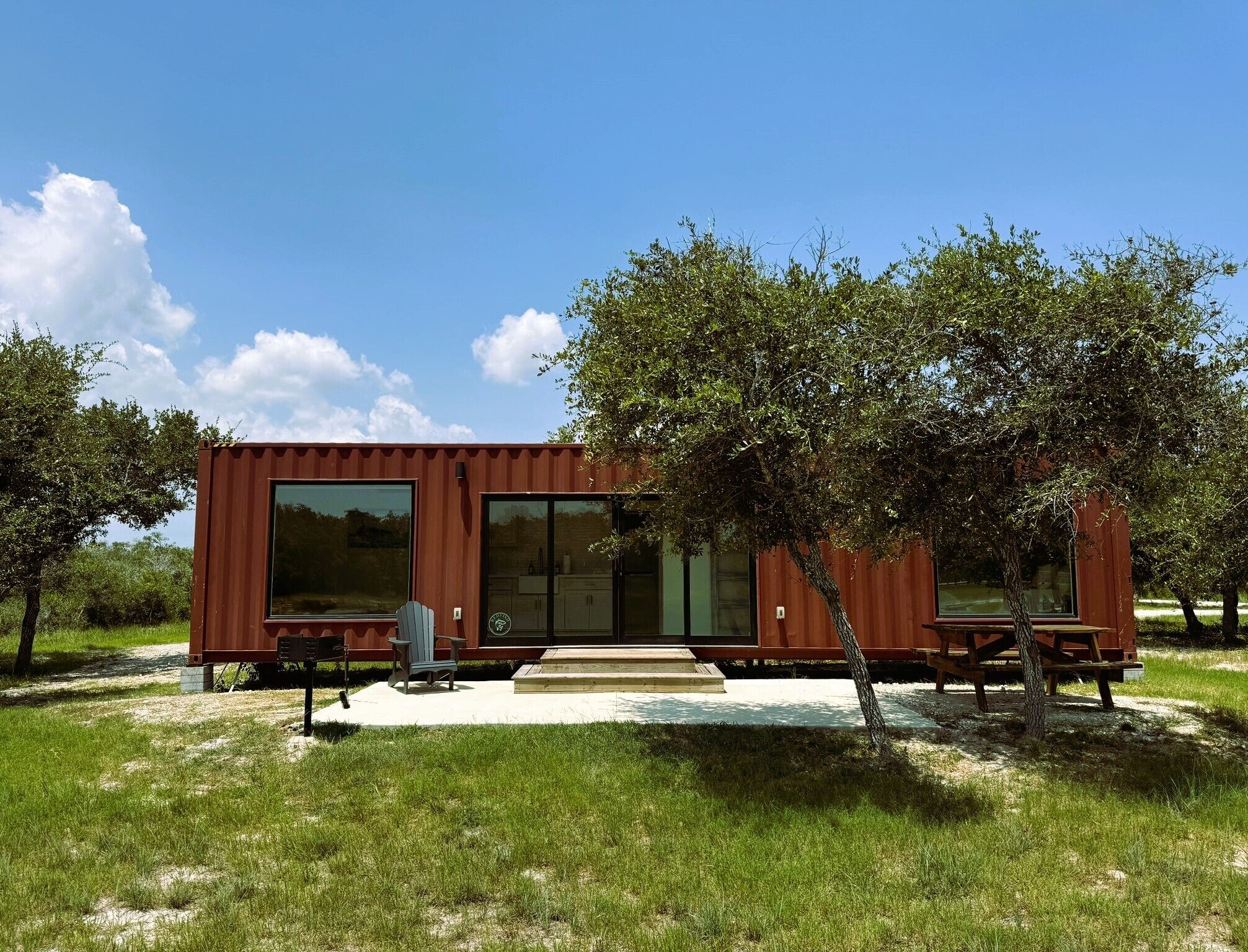 A modern, single-story house with a large sliding glass door, a small porch with a bench, and a tree in front.