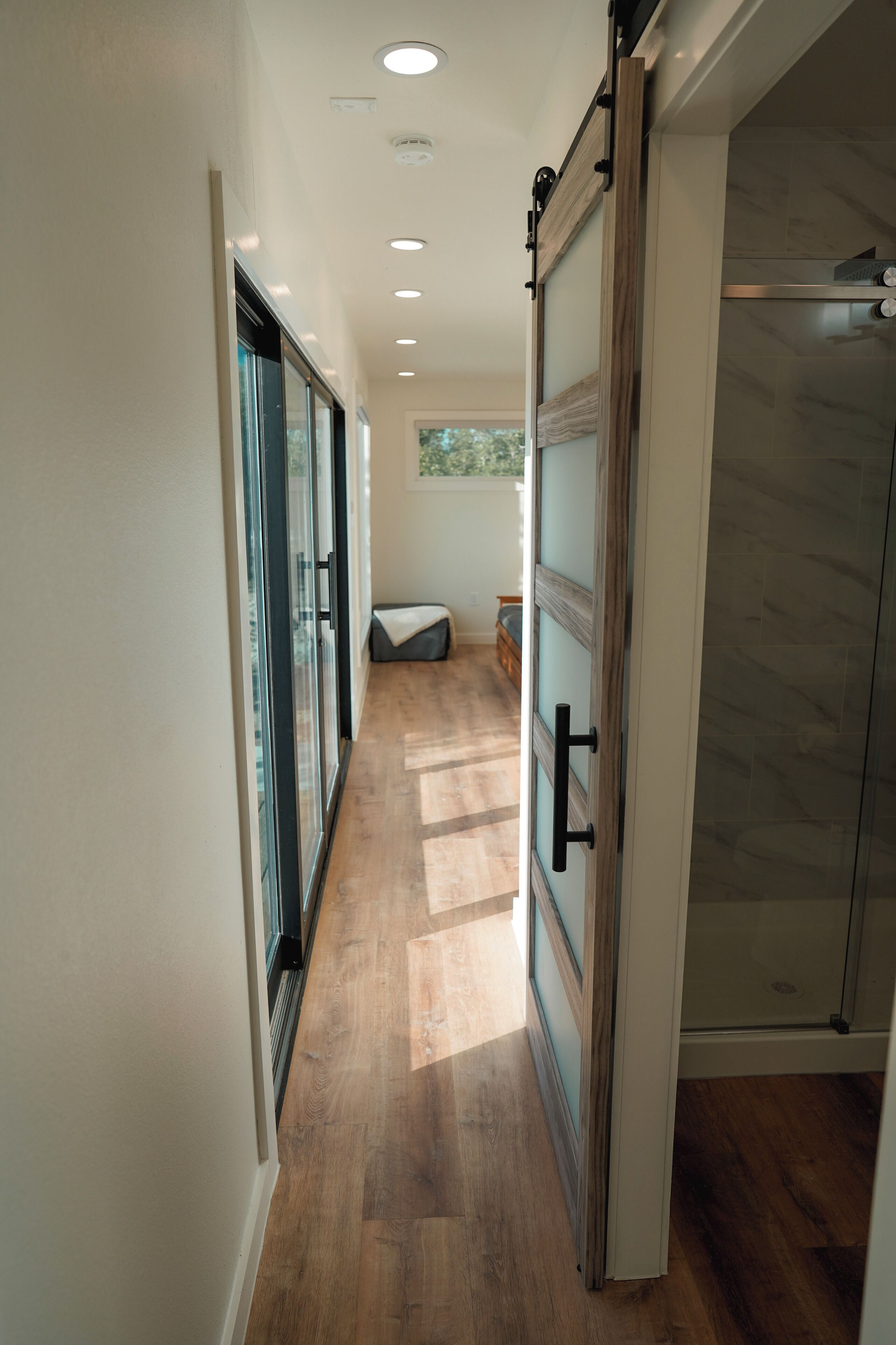 A hallway with wooden flooring, a sliding glass door, and a shower area.