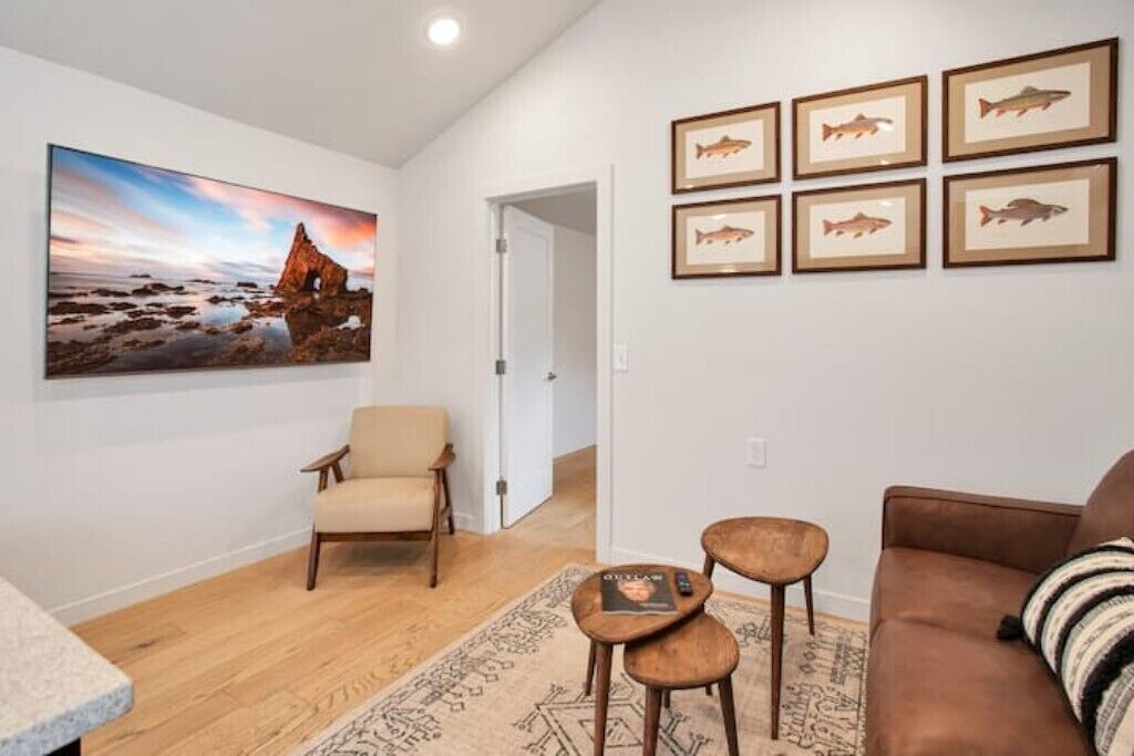 Un salon avec un fauteuil beige, un canapé marron, une table basse et un tapis. Des tableaux représentant des poissons, encadrés, ornent le mur.