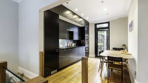 A modern kitchen with dark cabinetry, a wooden dining table, and a view through a glass door. - Stylish Kings Cross Apartment With Garden Retreat (London)