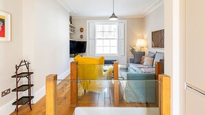 A modern living room with a glass partition, a yellow chair, a sofa, a TV, and a lamp. - Stylish Kings Cross Apartment With Garden Retreat (London)