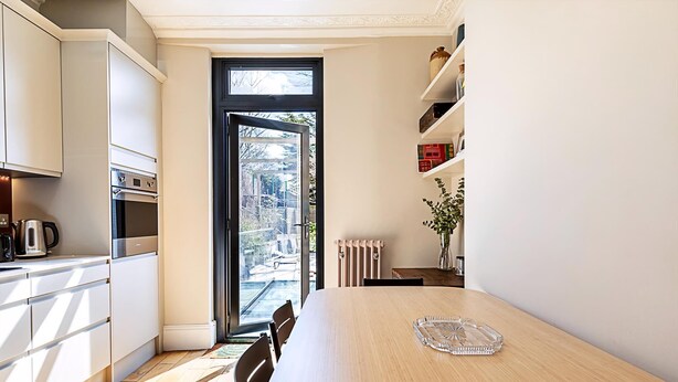 A modern kitchen with white cabinets, a large dining table, and a view through a glass door. - Stylish Kings Cross Apartment With Garden Retreat (London)