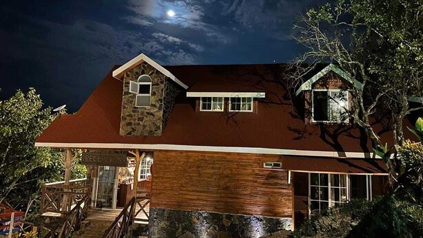 Un edificio de dos pisos con fachada de piedra y sección superior de madera, que presenta una escalera que conduce a una entrada cubierta.
