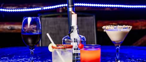 A bar setting with three drinks, a bottle, and a bottle opener.