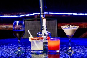 A bar setting with three drinks, a bottle, and a bottle opener.