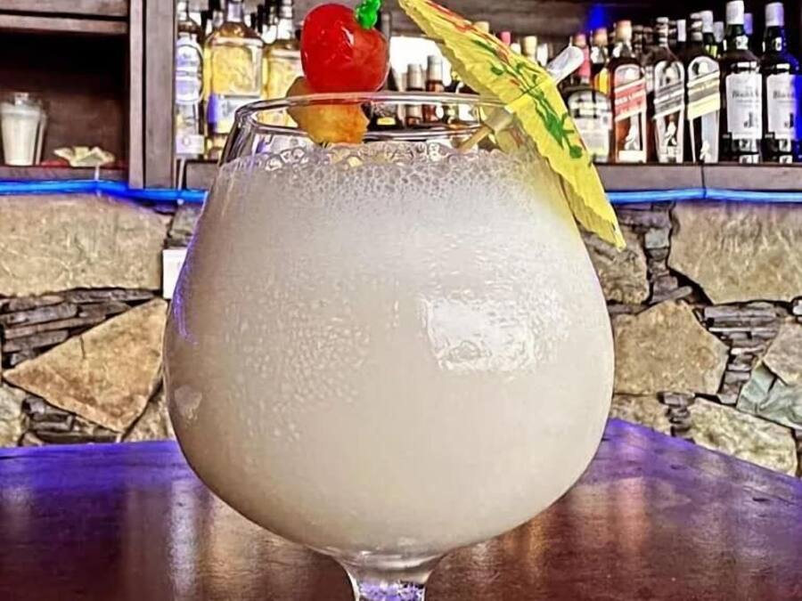 A cocktail in a glass with a straw and garnish on a bar counter.