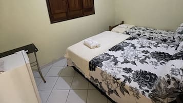 A bedroom with a bed, a desk, a chair, a window with shutters, an air conditioner, and a painting on the wall.