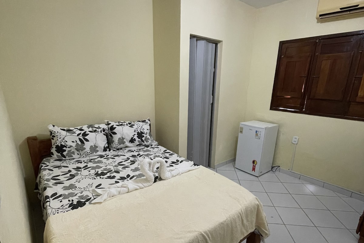 A bedroom with a bed, a small air conditioner, a door, and a window.
