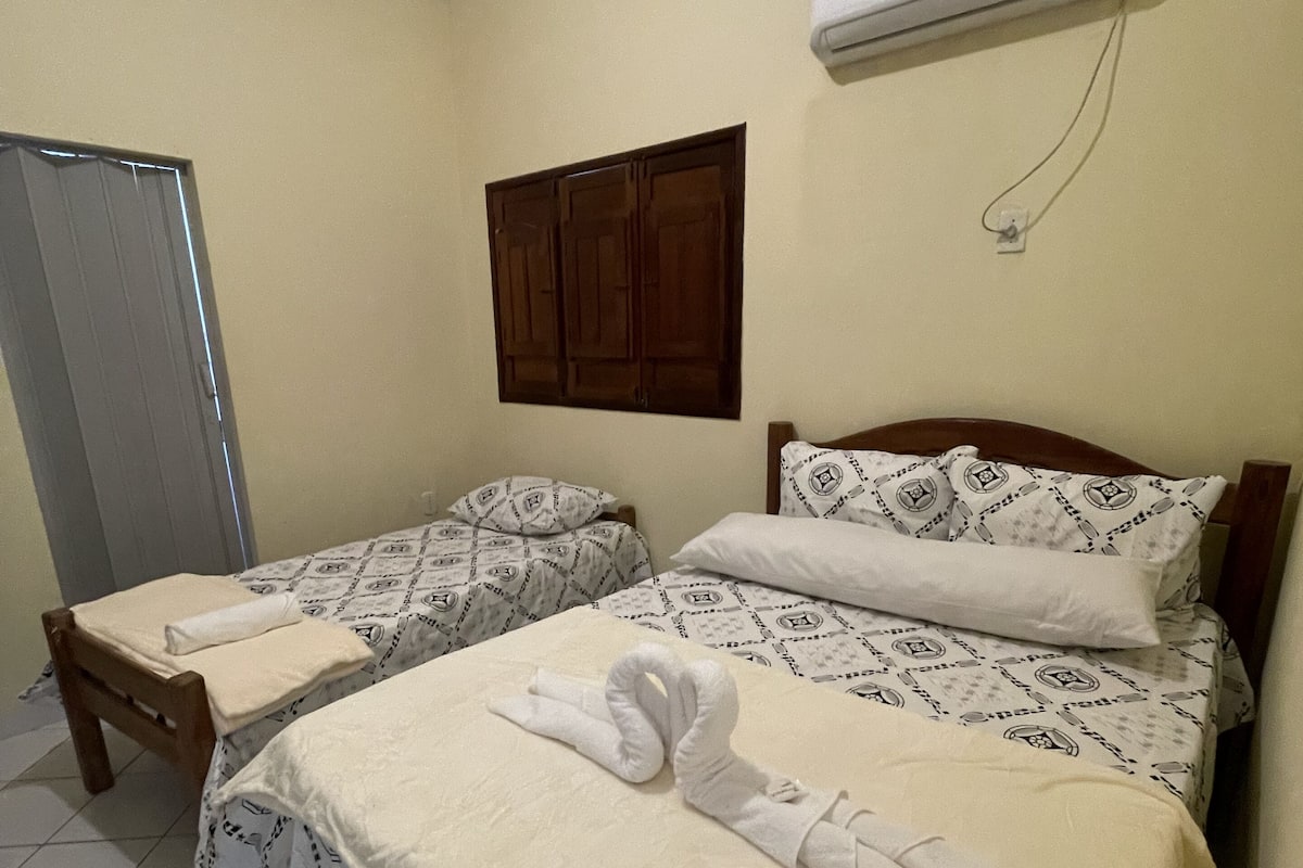 A hotel room with two beds, a wooden chair, a wardrobe, and an air conditioning unit.