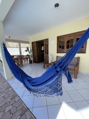 A hammock in a room with tiled flooring, wooden furniture, and a door leading to another room. - Pousada Praia do Francês (Marechal Deodoro)