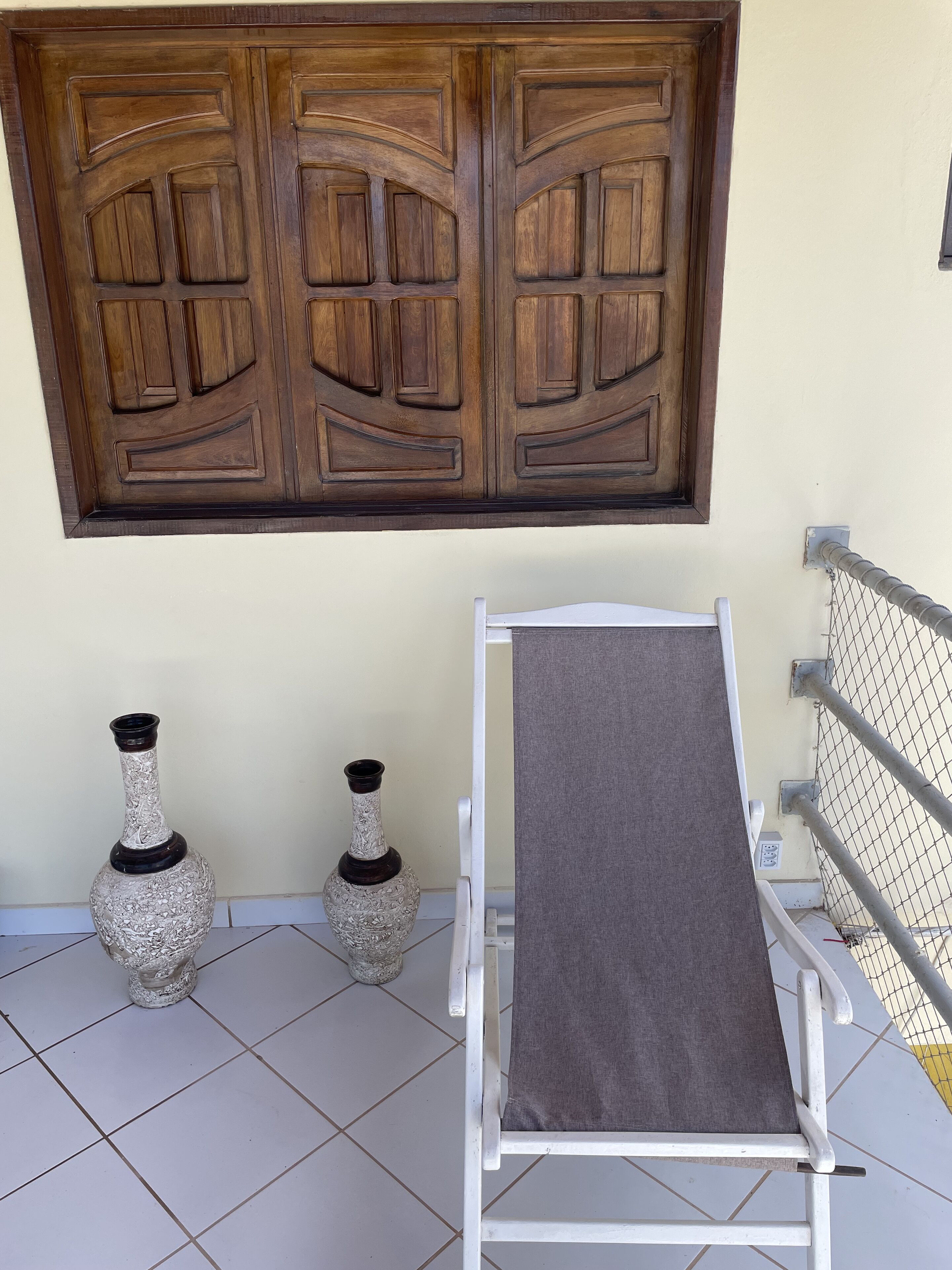 Una habitación con una puerta de madera grande, dos jarrones decorativos, un banco blanco y una barandilla de metal.