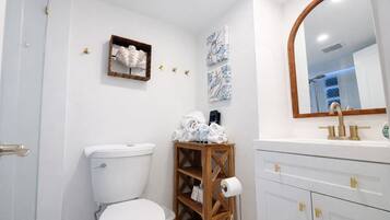 Une salle de bain comprenant des toilettes, une étagère en bois avec des serviettes, un miroir et un lavabo avec des robinets dorés.