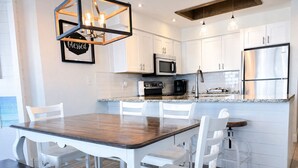 A modern kitchen with white cabinetry, a wooden dining table, and a built-in island with seating.