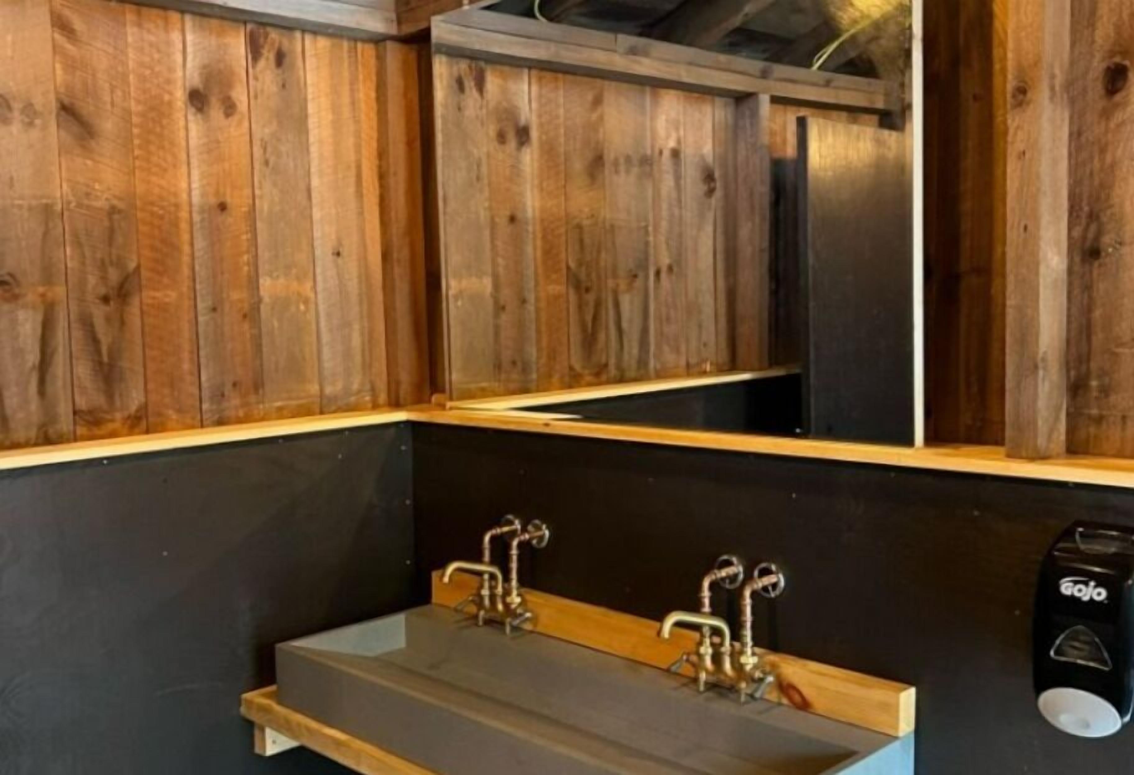 Une salle de bain avec des murs en bois, un comptoir noir et deux vasques dotées de robinets de style vintage.