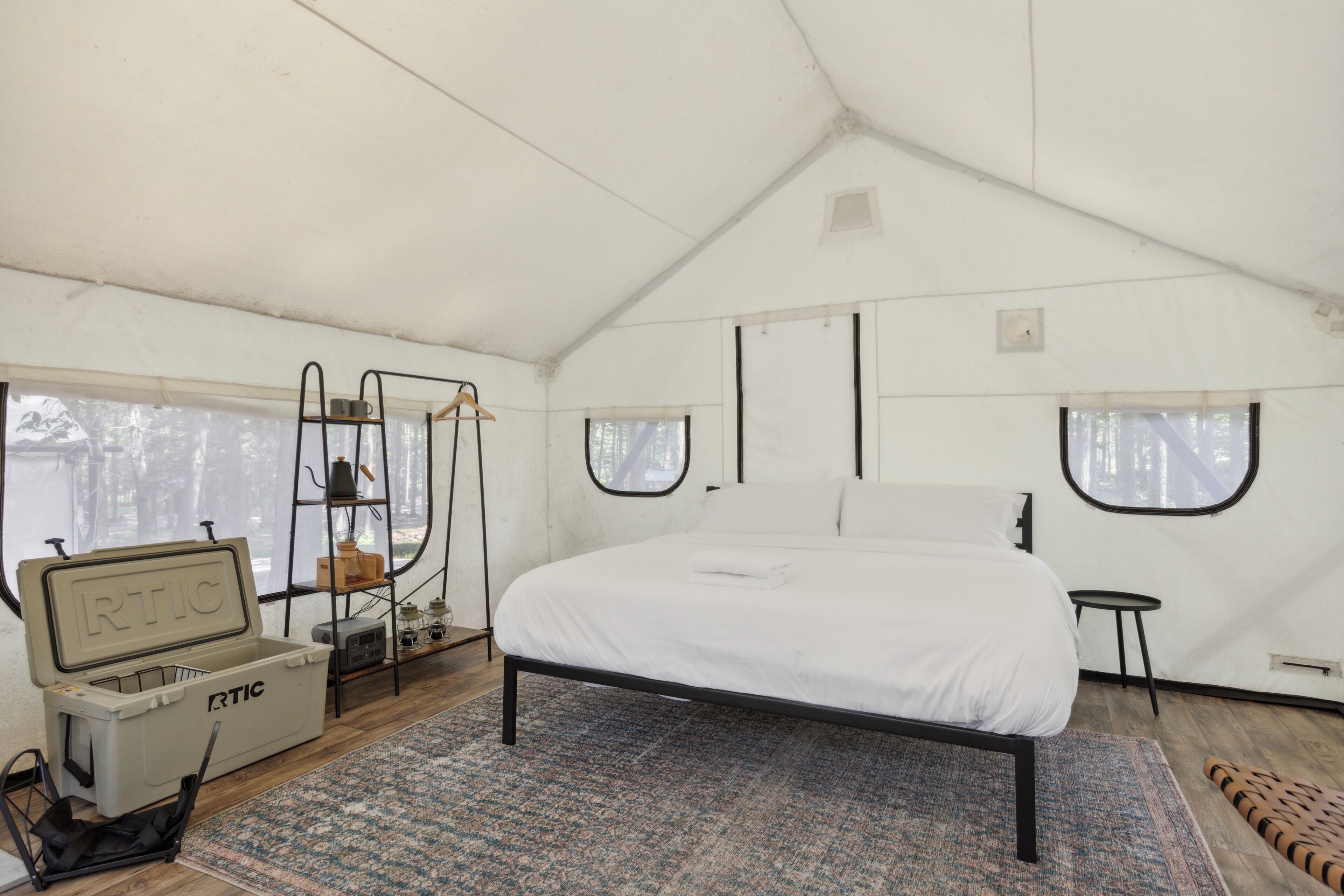 A tented room with a bed, a small table, a chair, and a storage unit with the label "RTIC".