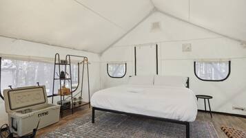 A tented room with a bed, a small table, a chair, and a storage unit with the label "RTIC".