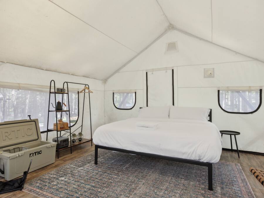 A tented room with a bed, a small table, a chair, and a storage unit with the label "RTIC".
