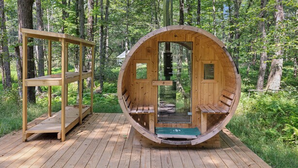 A wooden cabin with a circular structure, a wooden bench outside, and a wooden deck. - Ferncrest Campground (Greentown)